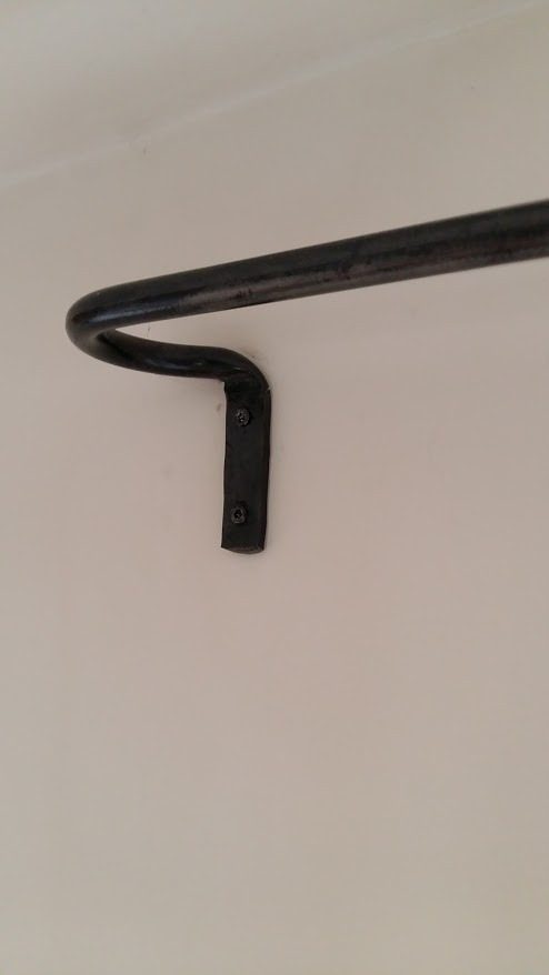 Support de tringle en fer forgé noir coudé fixé sur un mur blanc