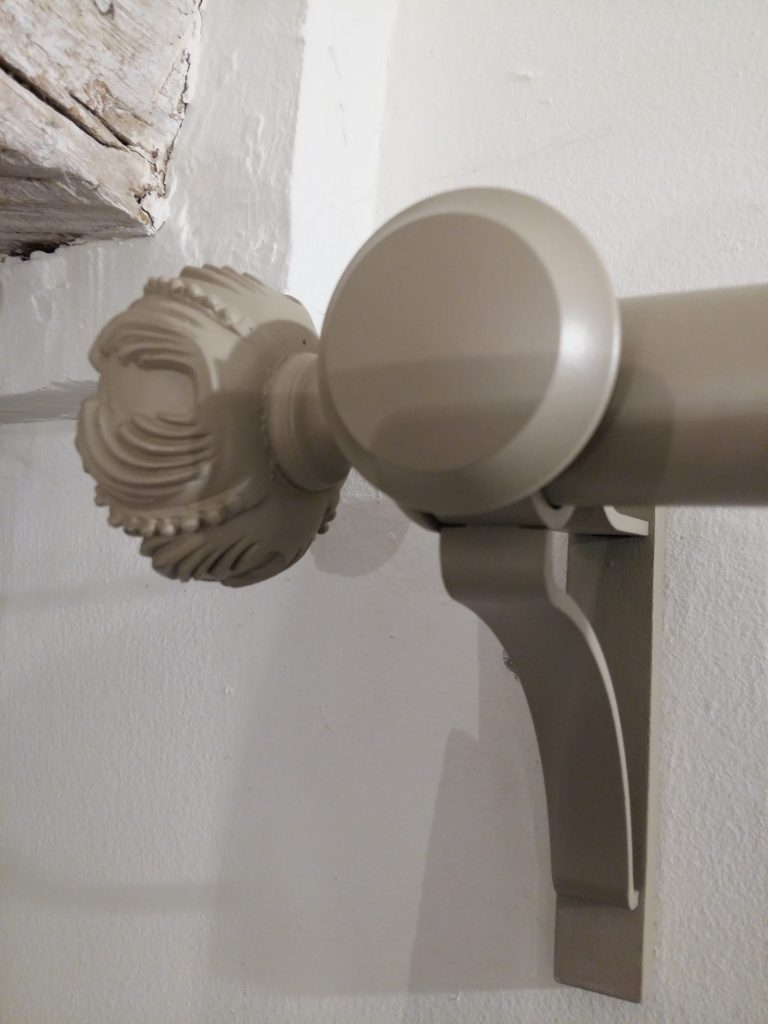 Embout sculpté et support de tringle en métal peint taupe fixés sur un mur blanc