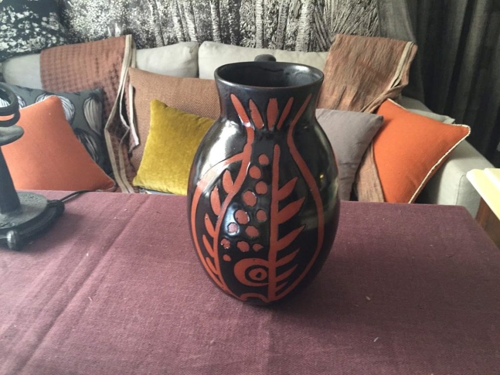 Vase en céramique noir et terracotta devant des coussins colorés