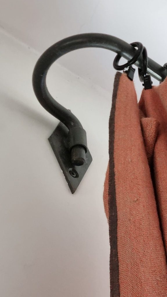 Support col-de-cygne en fer forgé noir fixé au mur, anneaux portant un rideau en lin terracotta